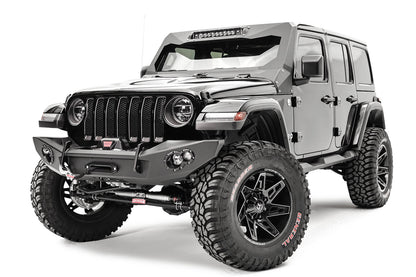 Fab Fours Lifestyle winch bumper on a gray Jeep Wrangler JL, driver-side front three-quarter view, showing the bumper with winch, red recovery hook strap and light pods