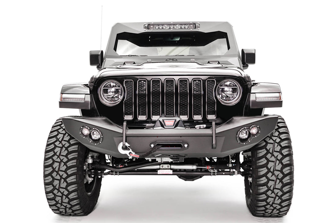 Fab Fours Lifestyle winch bumper on a white Jeep Wrangler JL, straight-on front view, showing the winch with red hook strap, tube hoop and round light pods