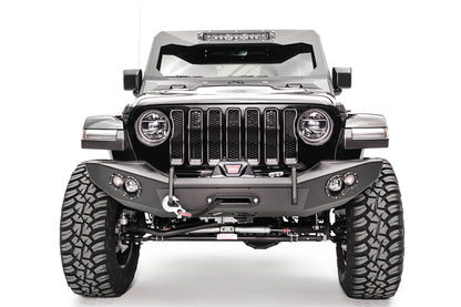 Fab Fours Lifestyle winch bumper on a white Jeep Wrangler JL, straight-on front view, showing the winch with red hook strap, tube hoop and round light pods