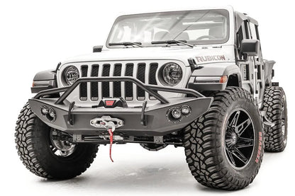 Fab Fours Lifestyle winch bumper with pre-runner guard on a white Jeep Wrangler JL, driver-side front three-quarter view, showing the tube hoop, winch with red hook strap and light pods