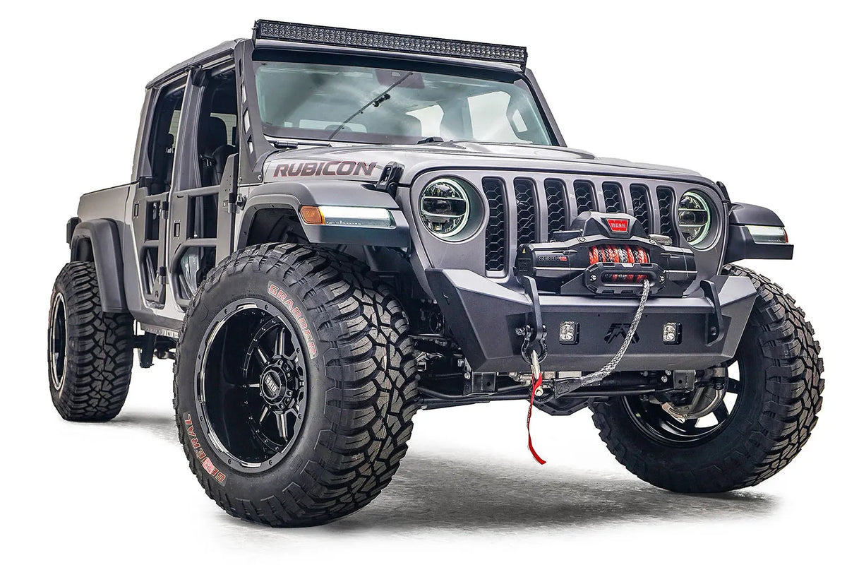 Fab Fours Stubby bumper on a gray Jeep Gladiator JT, passenger-side front three-quarter view, showing the compact bumper, winch with red hook and cube light openings