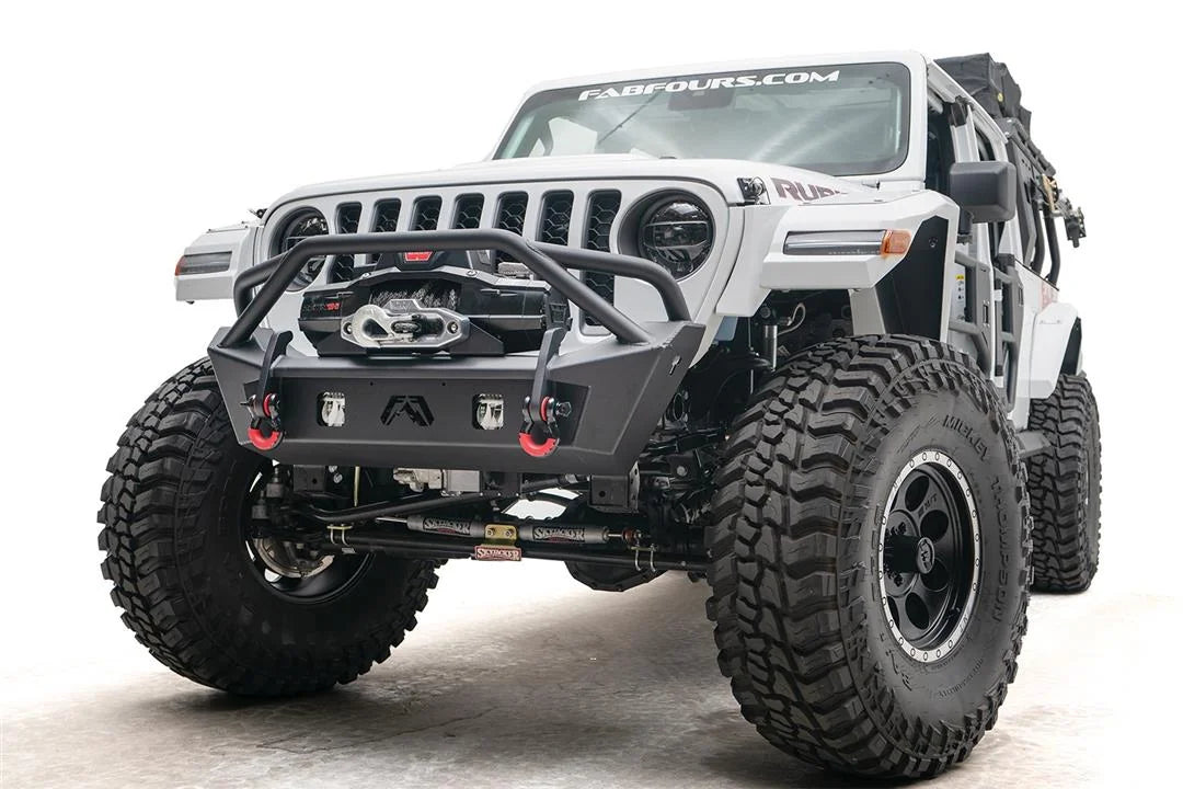 Fab Fours Stubby bumper with pre-runner guard on a white Jeep Wrangler JL, low driver-side front three-quarter view, showing the tube hoop, winch and red D-ring shackles