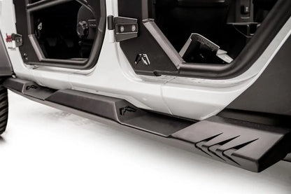 Fab Fours Light Rock Slider on a white Jeep Wrangler JL, low driver-side view, showing the flat black rocker guard with Fab Fours logo cutouts and chevron-cut rear end