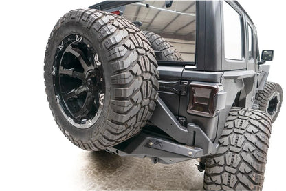 Fab Fours Off-The-Door Tire Carrier on a gray Jeep Wrangler JL, rear passenger-side view, holding an oversized spare on a frame-mounted arm beside the tailgate