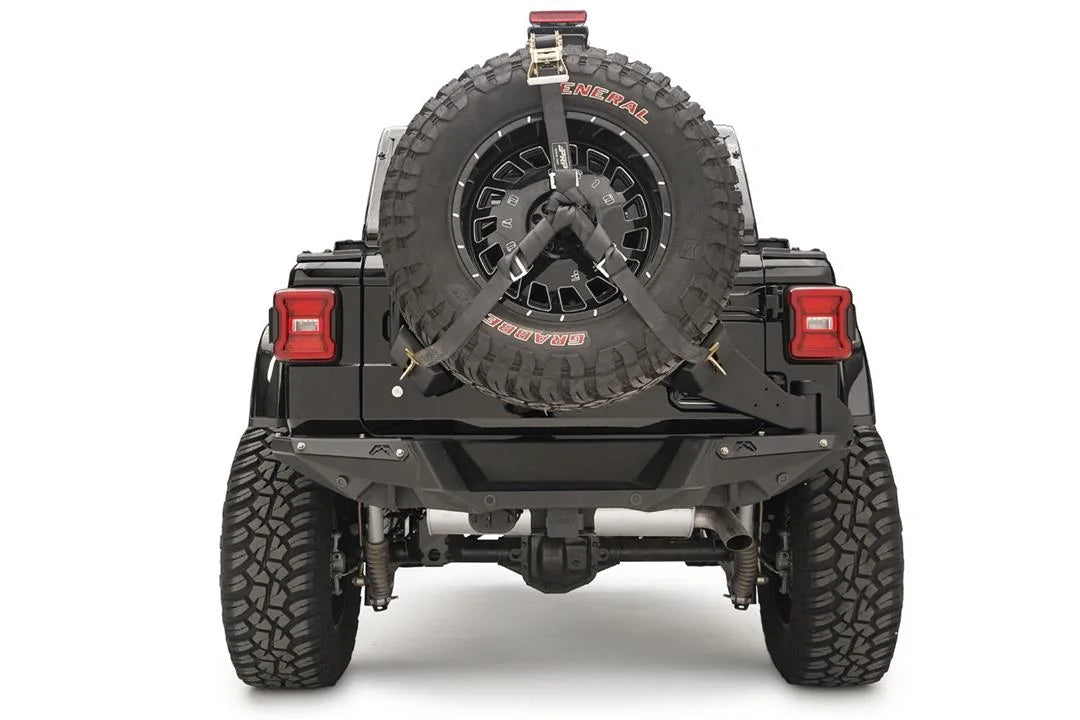 Fab Fours spare tire carrier on a black Jeep Wrangler JL, rear view, holding an oversized spare with ratchet straps and a raised third brake light