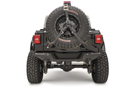 Fab Fours spare tire carrier on a black Jeep Wrangler JL, rear view, holding an oversized spare with ratchet straps and a raised third brake light