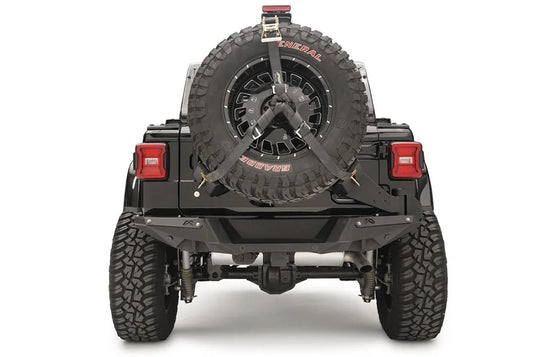 Fab Fours spare tire carrier on a black Jeep Wrangler JL, rear view, holding an oversized spare with ratchet straps and a raised third brake light