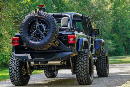 Fab Fours spare tire carrier on a black Jeep Wrangler JL on a gravel road, rear view