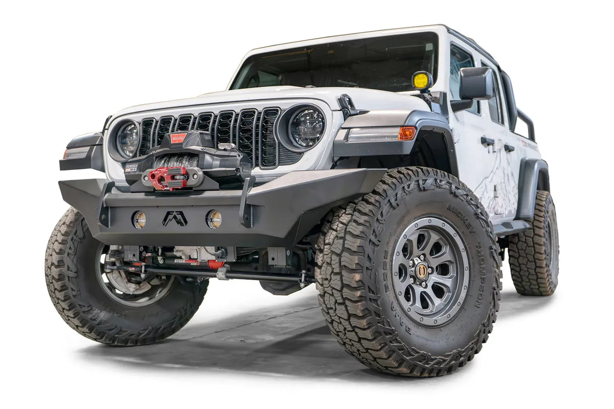 Fab Fours Premium front Lifestyle bumper on a white Jeep Wrangler JL, driver-side front three-quarter view, showing the full-width bumper, winch and integrated round lights