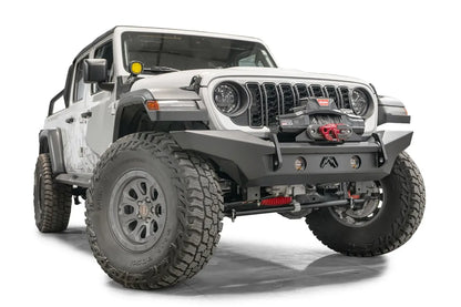 Fab Fours Premium front Lifestyle bumper on a white Jeep Wrangler JL, passenger-side front three-quarter view, showing the bumper, winch with red hook and round light pods