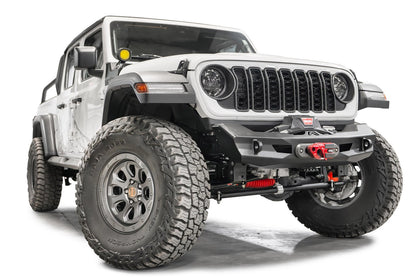 Fab Fours Ghost stubby front winch bumper with no guard on a lifted white Jeep Wrangler JL, front passenger-side view, showing the stubby bumper ends that clear the tires, the winch fairlead and the D-ring mounts