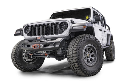 Fab Fours Ghost stubby front winch bumper with no guard on a lifted white Jeep Wrangler JL, front driver-side view, showing the compact faceted steel bumper with a centered winch and fairlead, Fab Fours logo and D-ring mounts