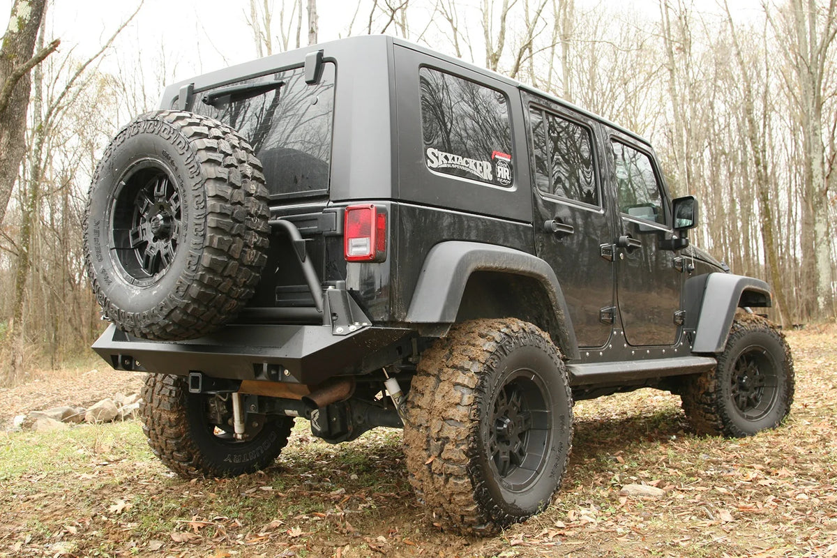 Fab Fours Swing-Away Tire Carrier and rear bumper on a black Jeep Wrangler JK Unlimited outdoors, rear passenger-side view with a mud-terrain spare mounted