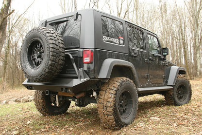 Fab Fours Swing-Away Tire Carrier and rear bumper on a black Jeep Wrangler JK Unlimited outdoors, rear passenger-side view with a mud-terrain spare mounted