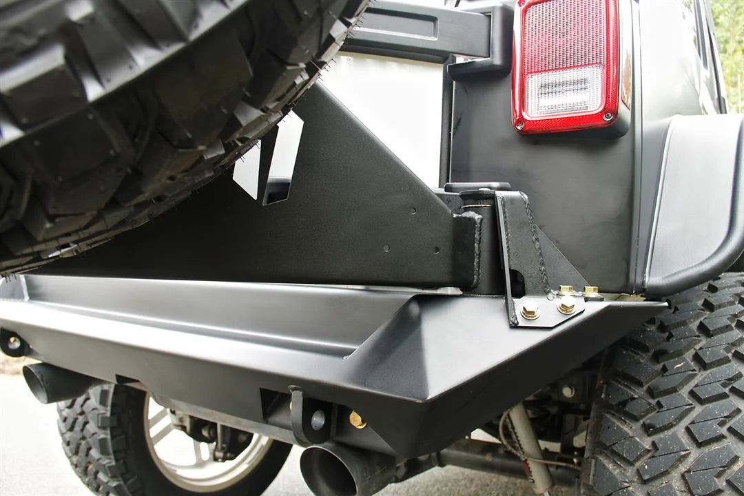 Fab Fours off-the-door tire carrier on a Jeep Wrangler JK, close-up of the swing arm pivot at the passenger-side corner of the Fab Fours rear bumper, with the carrier arm holding the spare tire