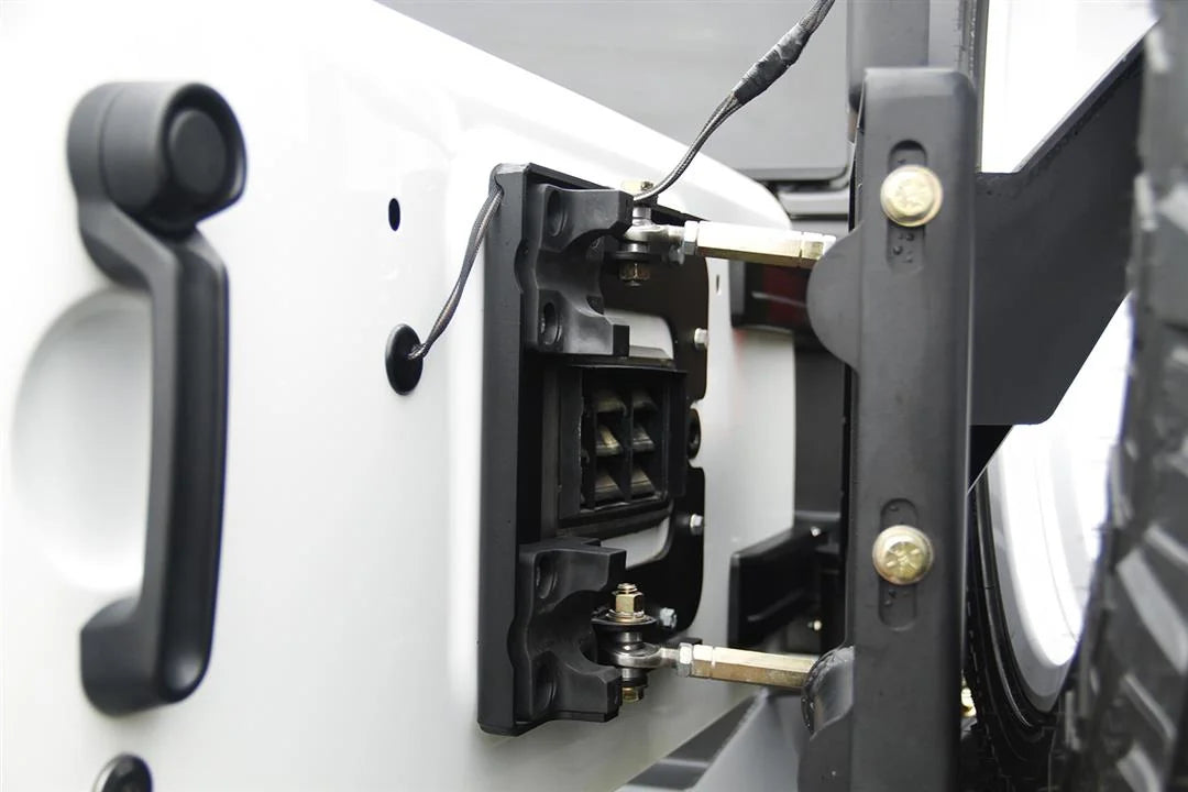 Fab Fours off-the-door tire carrier on a white Jeep Wrangler JK, close-up of the tailgate linkage, showing the adjustable rod ends connecting the carrier to the factory tailgate latch
