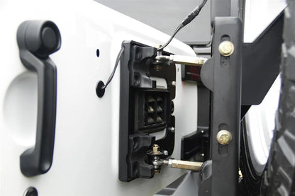 Fab Fours off-the-door tire carrier on a white Jeep Wrangler JK, close-up of the tailgate linkage, showing the adjustable rod ends connecting the carrier to the factory tailgate latch