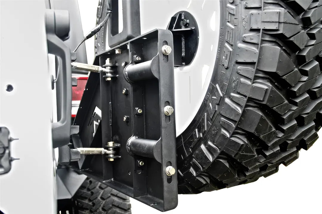 Fab Fours off-the-door tire carrier on a white Jeep Wrangler JK, close-up of the tire mount plate, showing the adjustable mounting slots, the linkage rods to the tailgate and the spare tire mounted to the carrier