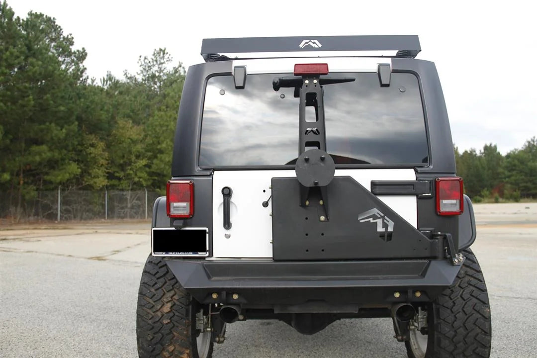 Fab Fours off-the-door tire carrier on a Jeep Wrangler JK, straight-on rear view, showing the swing-away carrier arm with the Fab Fours logo and the spare tire mount over a Fab Fours rear bumper