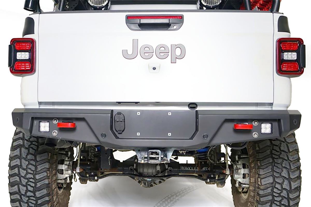 Close-up of Fab Fours standard rear bumper on a white Jeep Gladiator, straight rear view, with cube lights, red recovery points, parking sensors, and center license plate mount