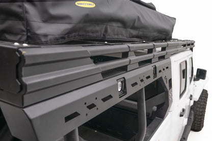 Close-up of the Fab Fours Overland Rack side rail on a white Jeep Gladiator, showing the slotted mounting panel, integrated cube light pods and tie-down points beneath a rooftop tent