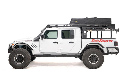 Fab Fours Overland Rack extension on a white Jeep Gladiator Rubicon, driver-side profile, showing the full-length rack from cab to bed with a rooftop tent and a jack mounted on the side