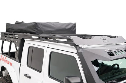 Fab Fours Overland Rack extension on a white Jeep Gladiator, passenger-side view, showing the matte black rack over the cab with LED light bars on the front fairing and a rooftop tent at the rear