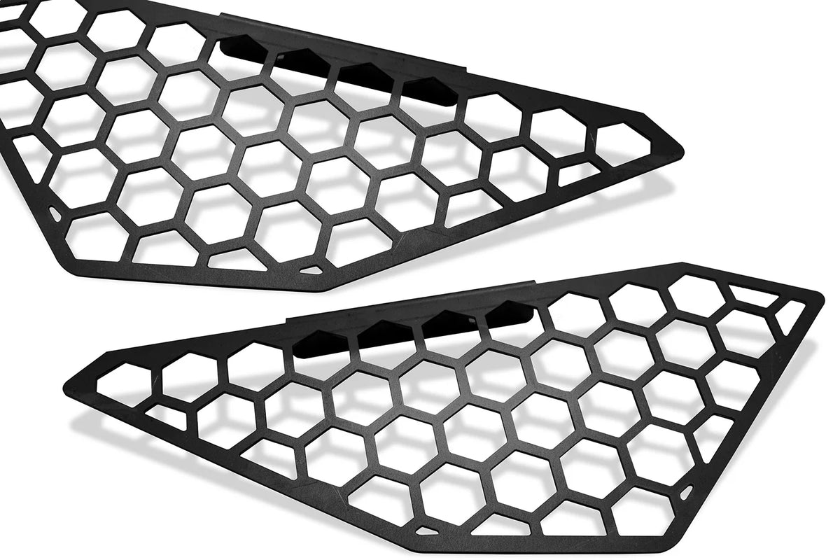 Fab Fours side light mesh insert covers for the Ford F-150 Vengeance bumper in black powder coat, pair shown at an angle, showing the honeycomb cut-out pattern and the angled mounting tabs on each cover