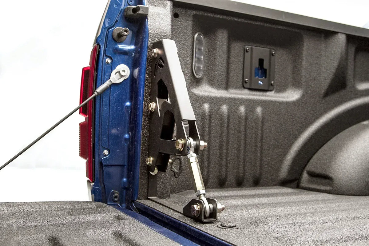 Fab Fours truck bed brace on a blue pickup, close-up of the steel bracket bolted to the bed wall with an adjustable rod end linking it to the bed floor beside the tailgate