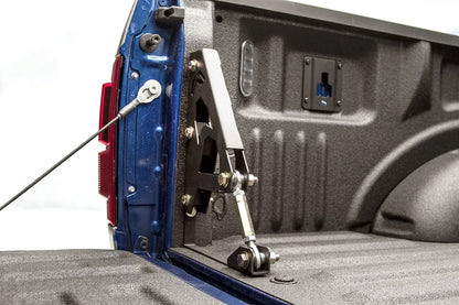 Fab Fours truck bed brace on a blue pickup, close-up of the steel bracket bolted to the bed wall with an adjustable rod end linking it to the bed floor beside the tailgate