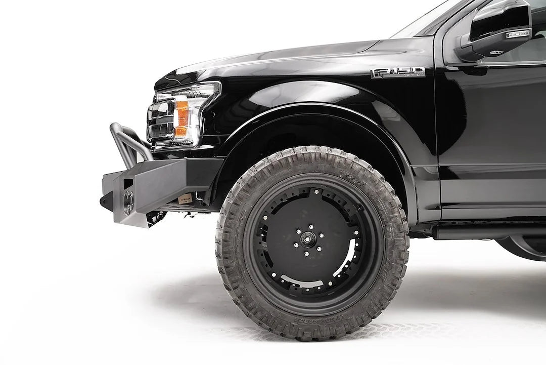 Fab Fours Premium winch front bumper with pre-runner guard on a black Ford F-150, driver-side profile view of the bumper end and front wheel