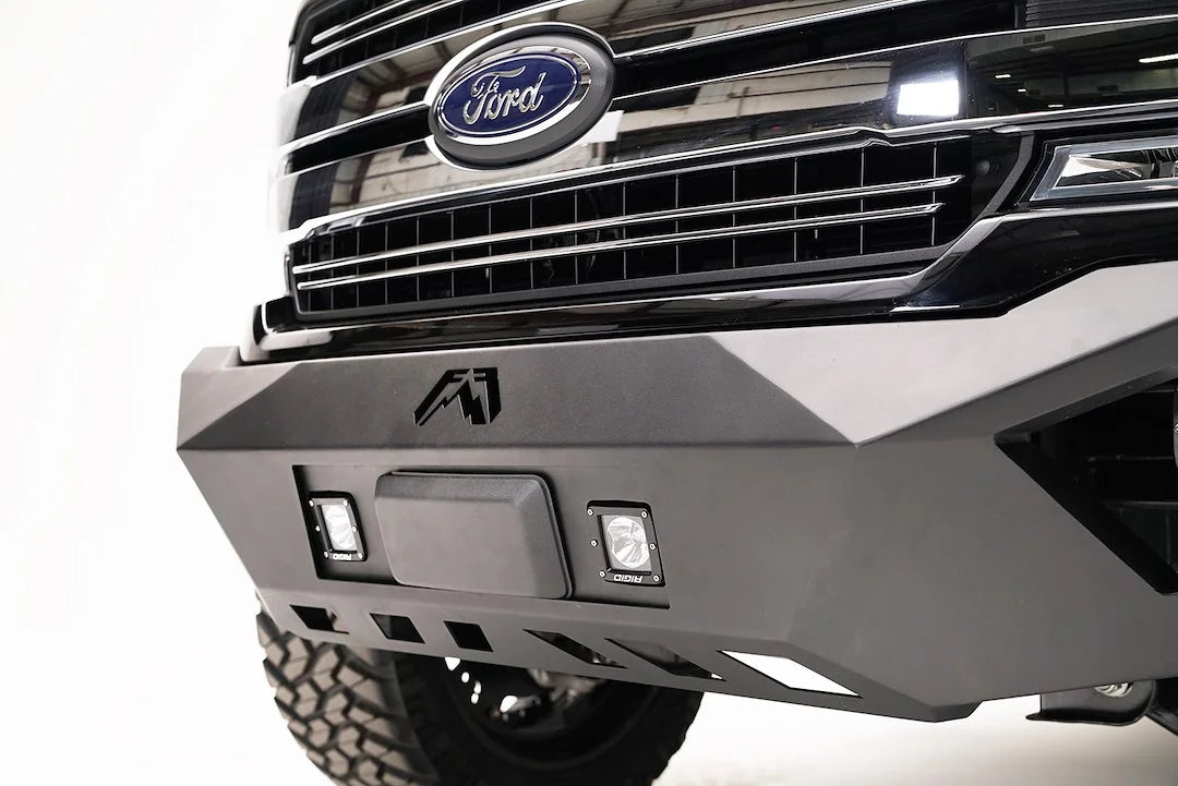 Fab Fours adaptive cruise control relocation bracket in a Fab Fours front bumper on a black Ford F-150, driver-side close-up, with the radar sensor between two cube lights