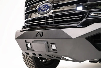 Fab Fours adaptive cruise control relocation bracket in a Fab Fours front bumper on a black Ford F-150, driver-side close-up, with the radar sensor between two cube lights