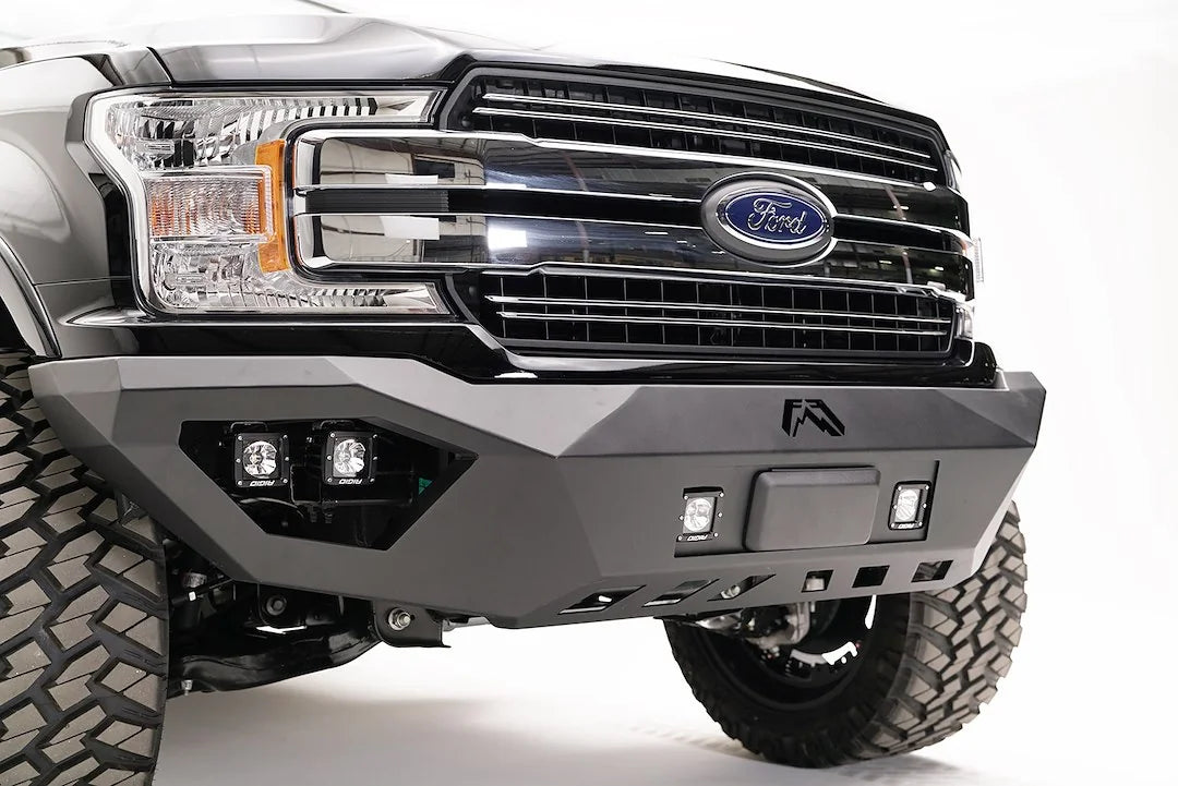 Fab Fours adaptive cruise control relocation bracket mounted in the center of a Fab Fours front bumper on a black Ford F-150, passenger-side front three-quarter view, with the radar sensor between two cube lights
