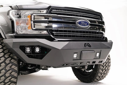 Fab Fours adaptive cruise control relocation bracket mounted in the center of a Fab Fours front bumper on a black Ford F-150, passenger-side front three-quarter view, with the radar sensor between two cube lights