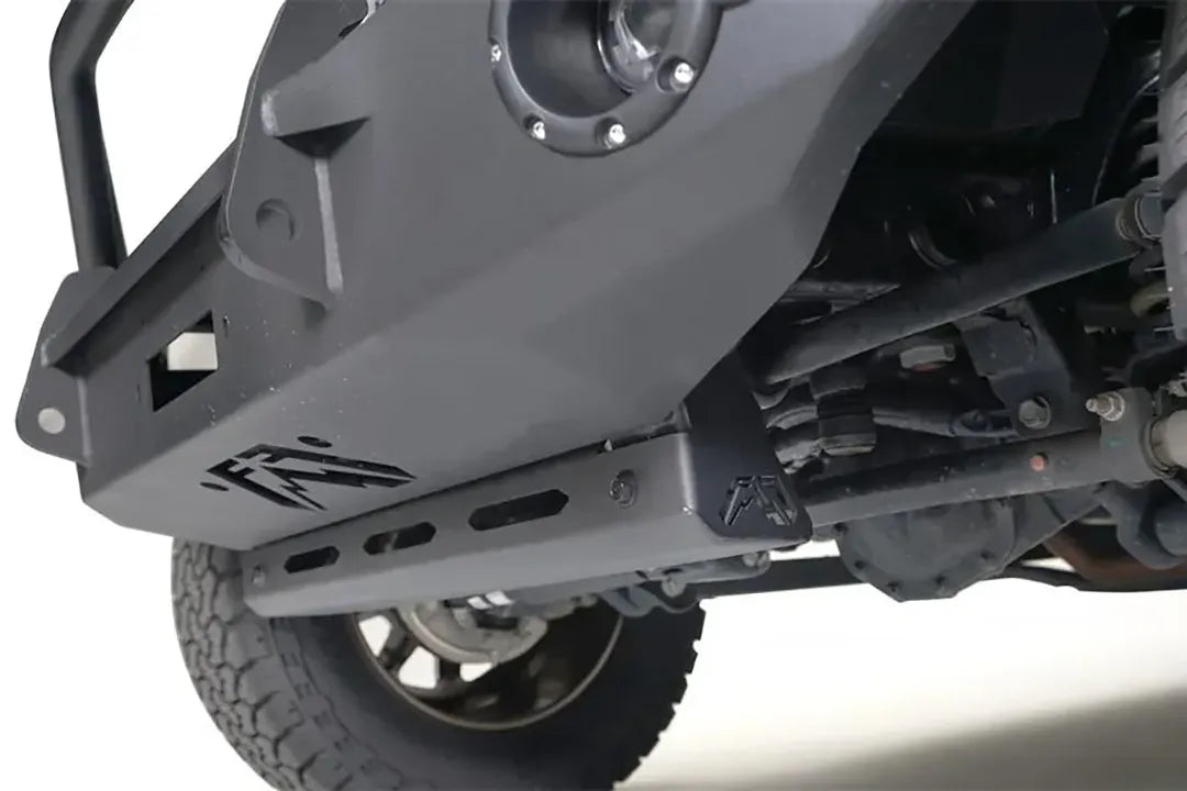 Close-up of the Fab Fours sway bar cover on a Jeep Wrangler JL, showing the matte black slotted steel guard with Fab Fours logo bolted beneath the front bumper