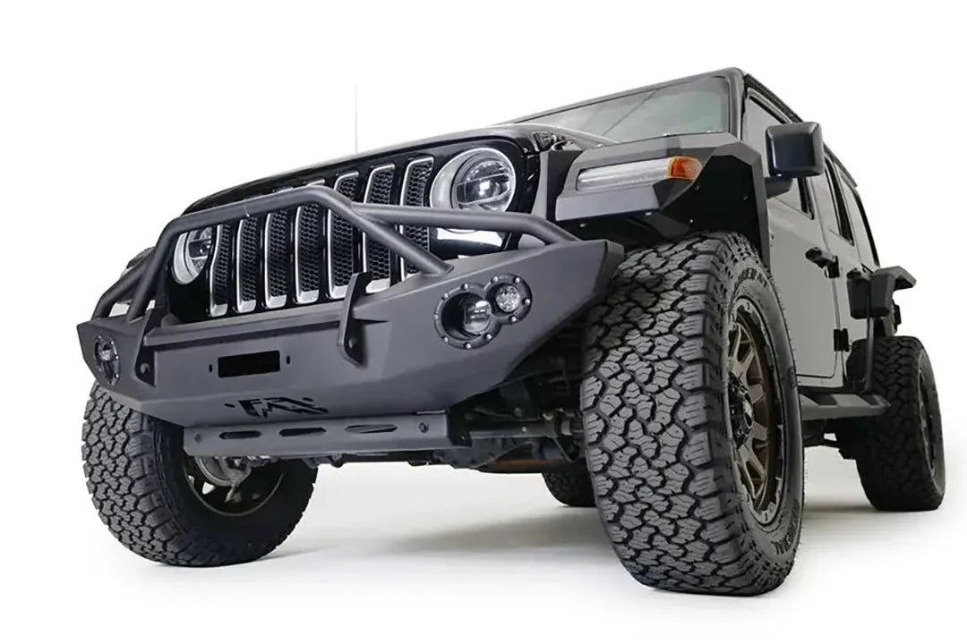 Fab Fours sway bar cover on a black Jeep Wrangler JL, low front driver-side view, showing the slotted steel cover protecting the front sway bar below a Fab Fours front bumper