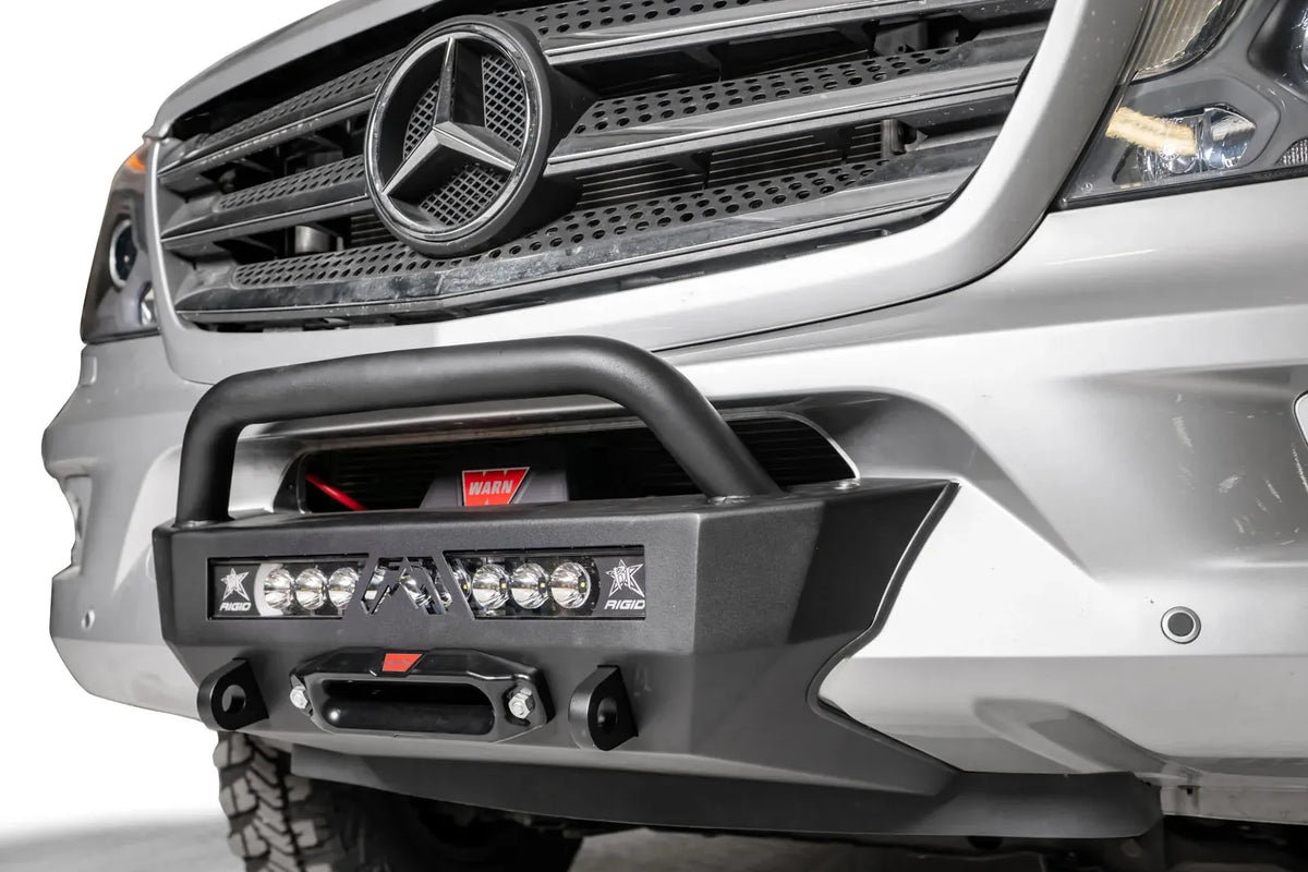 Fab Fours semi-hidden winch mount with pre-runner guard on a silver Mercedes-Benz Sprinter, close-up angle, showing the tube hoop, winch, light bar and fairlead