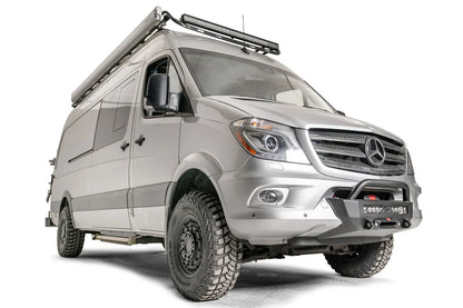 Fab Fours semi-hidden winch mount with pre-runner guard on a silver Mercedes-Benz Sprinter, passenger-side front three-quarter view, showing the tube hoop, light bar and winch plate