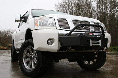 Fab Fours winch mount on a white Nissan TITAN outdoors, passenger-side front three-quarter view, showing the tube hoop, winch and roller fairlead