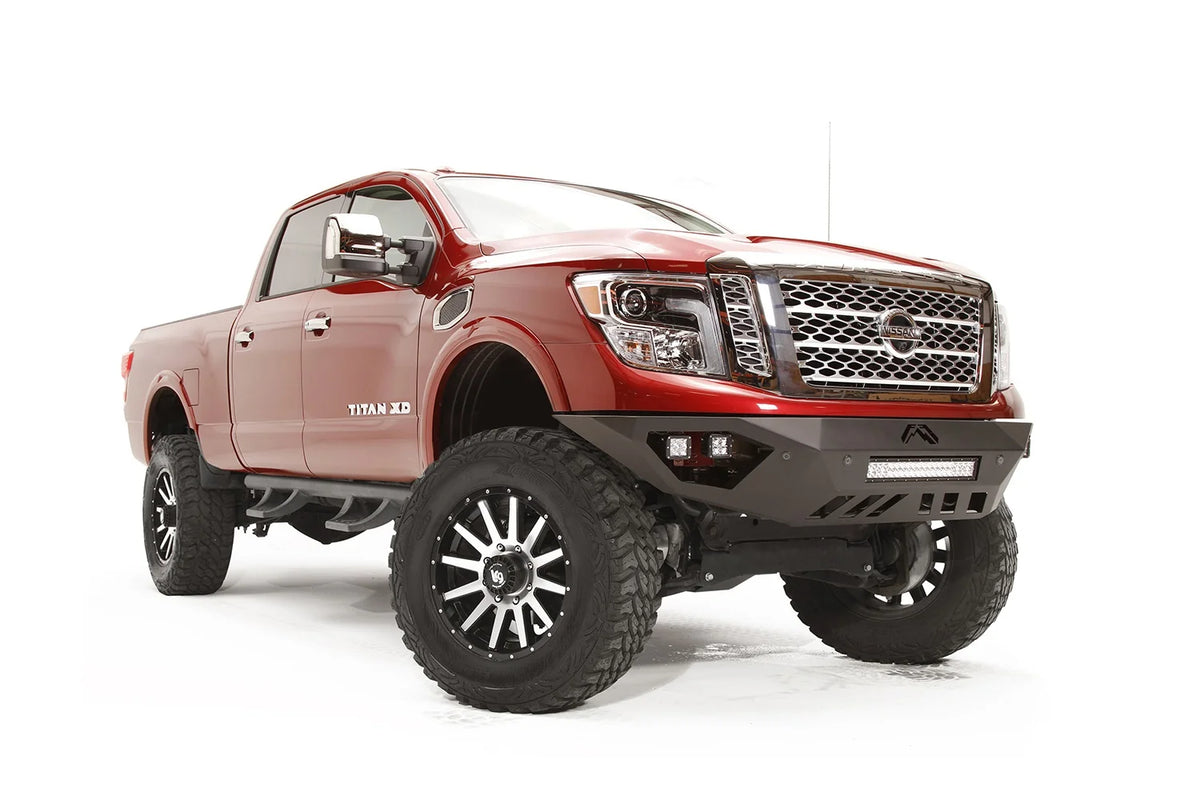 Fab Fours Vengeance front bumper on a red Nissan TITAN XD, passenger-side front three-quarter view, showing the angular bumper, LED light bar and cube lights