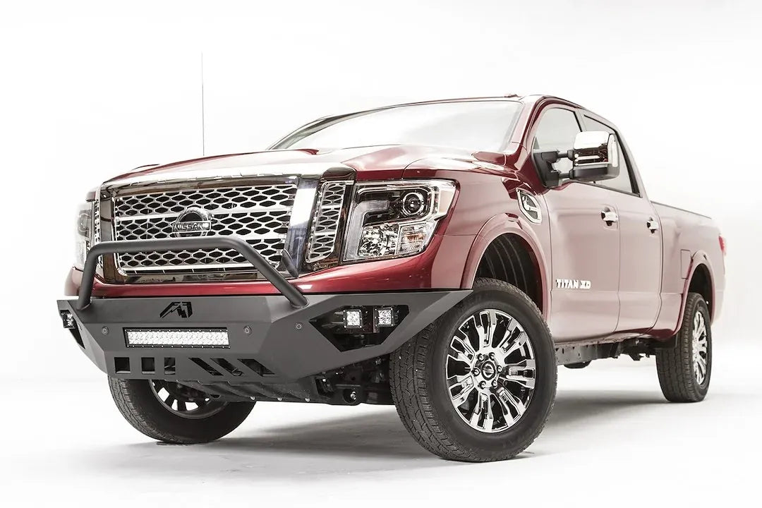 Fab Fours Vengeance front bumper with pre-runner guard on a red Nissan TITAN XD, driver-side front three-quarter view, showing the tube hoop, LED light bar and cube lights