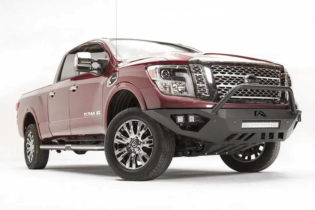 Fab Fours Vengeance front bumper with pre-runner guard on a red Nissan TITAN XD, passenger-side front three-quarter view, showing the tube hoop, LED light bar and cube lights