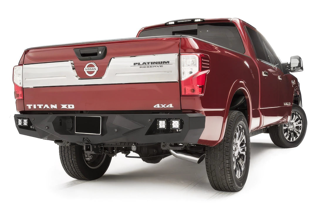 Fab Fours Vengeance rear bumper on a red Nissan Titan XD, passenger-side rear three-quarter view, with dual cube lights in each corner, center license plate area, and hitch receiver