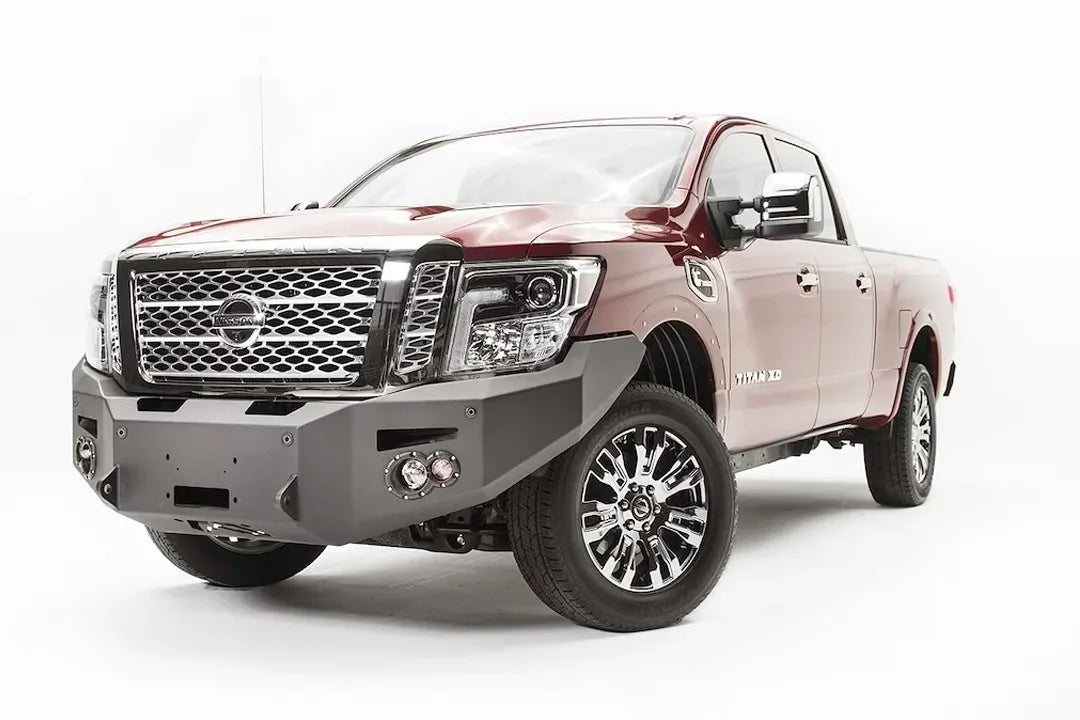 Fab Fours Premium front bumper on a red Nissan TITAN XD, driver-side front three-quarter view, showing the full-width bumper, winch opening and round fog light pods