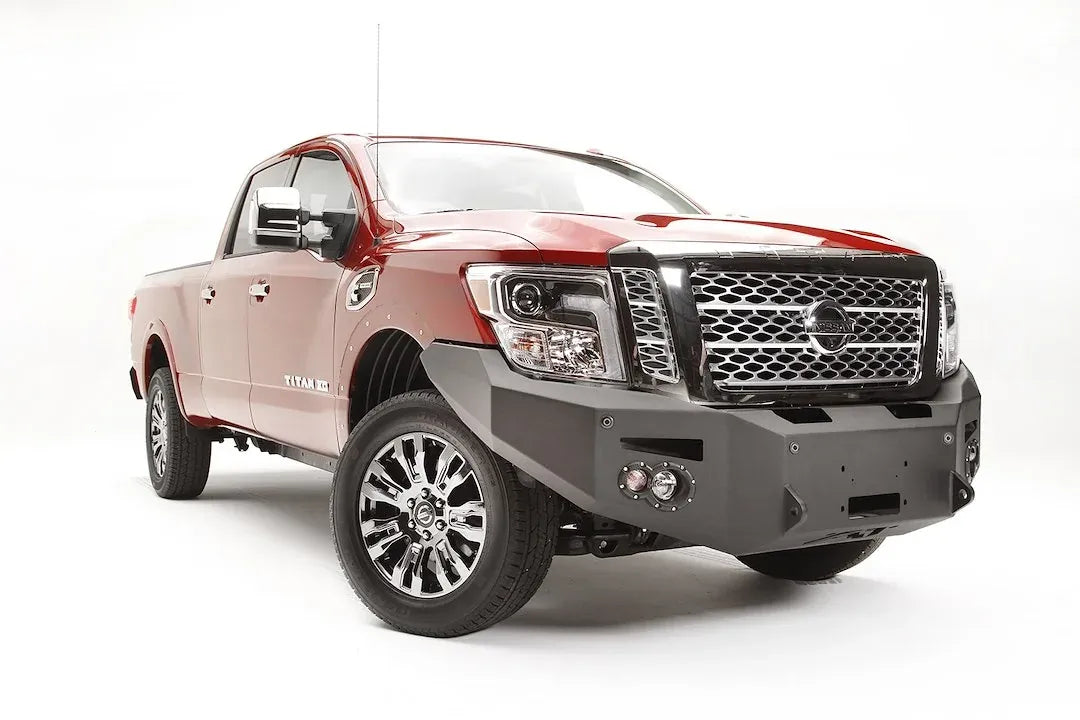 Fab Fours Premium front bumper on a red Nissan TITAN XD, passenger-side front three-quarter view, showing the full-width bumper, winch opening and round fog lights