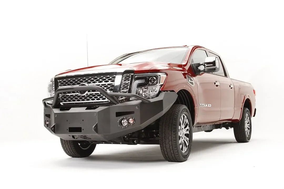 Fab Fours Premium front bumper with pre-runner guard on a red Nissan TITAN XD, driver-side front three-quarter view, showing the tube hoop, winch opening and round fog lights