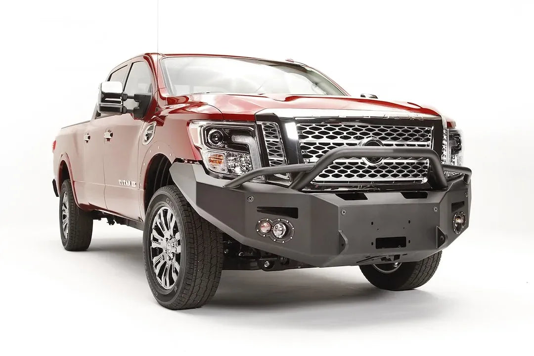 Fab Fours Premium front bumper with pre-runner guard on a red Nissan TITAN XD, passenger-side front three-quarter view, showing the tube hoop, winch opening and round fog lights
