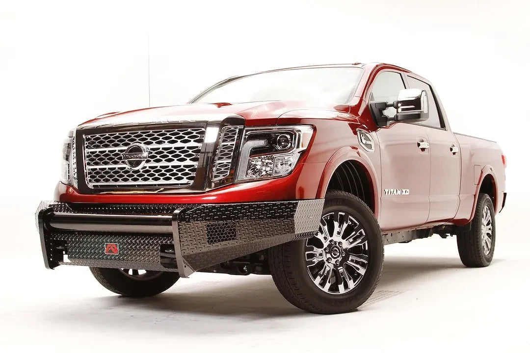 Fab Fours Black Steel front bumper on a red Nissan TITAN XD, passenger-side front three-quarter view, showing the diamond-plate bumper, wraparound ends and light openings