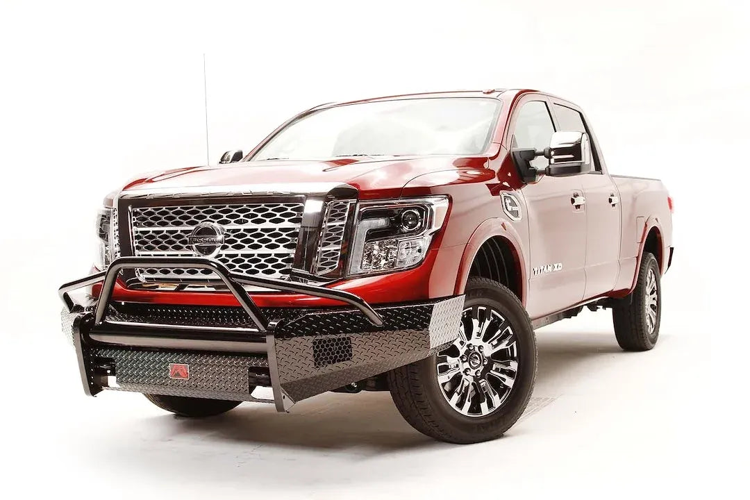 Fab Fours Black Steel front bumper with pre-runner guard on a red Nissan TITAN XD, passenger-side front three-quarter view, showing the tube hoop, diamond-plate bumper and light openings